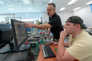 A student at a desk in front of a student being instructed by the teacher